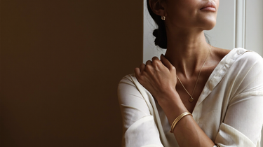 Woman in an ivory silk shirt wearing a fine gold chain necklace, small gold hoop earrings and thin gold bangles