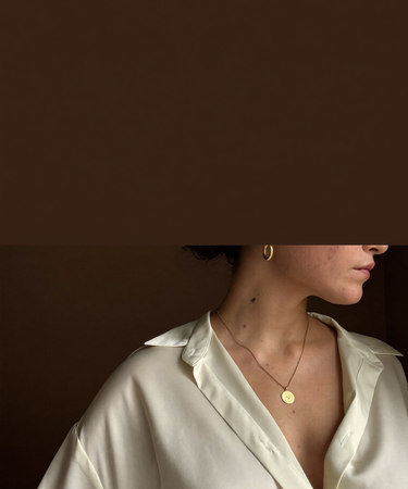 Woman in an ivory silk shirt wearing a fine gold chain necklace and small gold hoop earrings